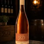 Flasche Rosé Frizzante Jahrgang 2025 auf dunklem Schiefer in einem Weinkeller.